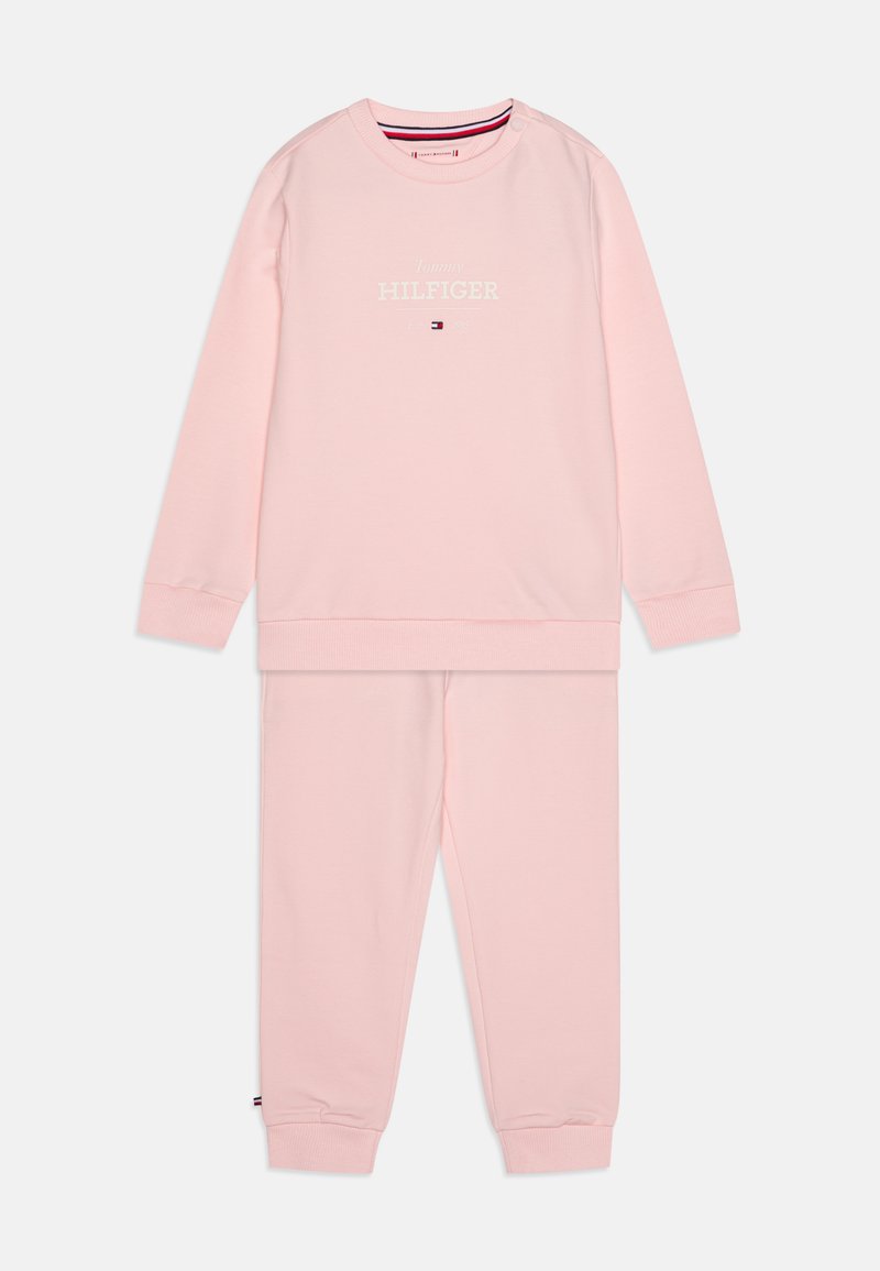 Sweatshirt de algodão rosa claro com decote redondo e punhos canelados, apresentando o logótipo branco "Tommy Hilfiger" na frente. Calças de fato rosa em combinação.