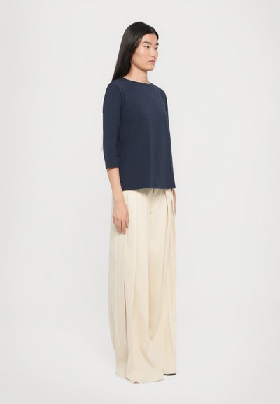 Top blu navy a tre quarti abbinato a pantaloni a vita alta, larghi, di colore crema. Tessuto morbido con una vestibilità rilassata.