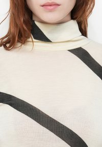Maglione a collo alto beige chiaro con strisce diagonali grigio scuro. Tessuto morbido e testurizzato; design aderente che enfatizza il collo e i motivi.