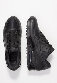 Czarne sneakersy Nike Air Max 90 charakteryzują się cholewką z mieszanych materiałów, w tym gładkiej skóry i teksturowanej tkaniny. Podeszwa ma wyraźne rowki zapewniające przyczepność oraz widoczną jednostkę powietrzną.