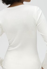 Woman wearing a plain white long-sleeve shirt shown from the back with curly hair partially visible.