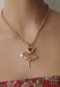 Goldkette mit herzförmigen Anhängern; einer mit rotem Stein, zwei mit Perlen und einem Schlüsselschlüsselanhänger. Komplexe Details throughout.