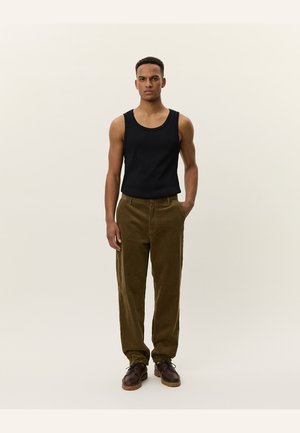Black sleeveless tank top paired with olive green corduroy pants. Brown lace-up shoes complete the outfit, showcasing a relaxed fit.