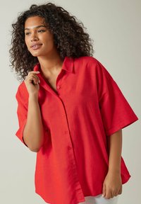 Camisa de botones de manga corta roja con cuello, hecha de una tela ligera, que presenta un corte relajado y detalles de botones visibles.