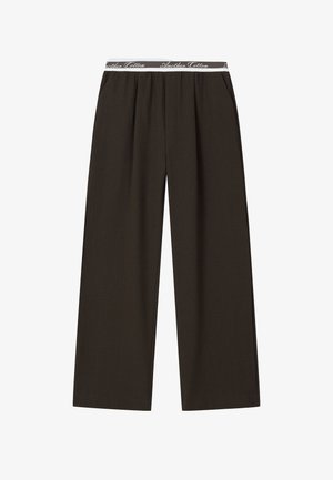 Tumedpruunid laial jalaga püksid, millel on elastne vöökoht ja valge kirjaga "Another Cotton" tekst kordub selle ümber.