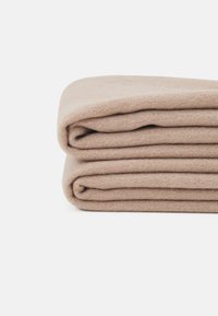 Couverture en laine beige pliée avec une texture douce, de forme rectangulaire, et des plis soigneusement superposés, affichant une couleur uniforme et une surface lisse.