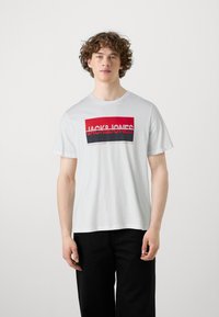 T-shirt in cotone bianco con stampa grafica in rosso e nero con la scritta "JACK & JONES." Maniche corte e scollatura rotonda, abbinato a pantaloni neri.
