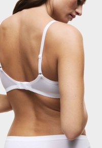 Sujetador blanco con tirantes ajustables, tela texturizada, bordes con forma de ondas y cierre de gancho y ojo en la parte posterior, emparejado con ropa interior blanca a juego.