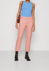 Helle rosa maßgeschneiderte Hose mit Seitentaschen, kombiniert mit einem blauen Ripp-Top. Dazu gehören schwarze Knöchelstiefel und eine bordeauxfarbene Handtasche.