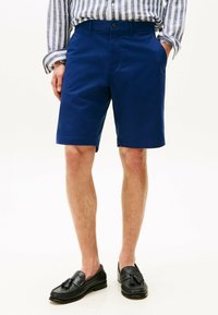Marineblauwe katoenen shorts met een rechte snit, voorzakken en een knoopsluiting, gecombineerd met zwarte instappers en een gestreept shirt.