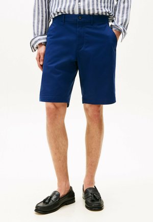 Marineblauwe katoenen shorts met een rechte snit, voorzakken en een knoopsluiting, gecombineerd met zwarte instappers en een gestreept shirt.