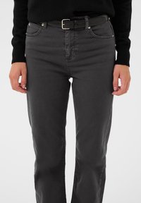 Čierne denimové rifle so štandardným strihom, dizajnom s piatimi vreckami, rovnomernou textúrou a čiernym opaskom so striebornou sponou.