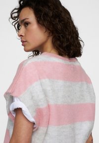 Suéter de punto a rayas en suave rosa y gris. Presenta un escote redondo, amplios agujeros para los brazos y un logo bordado en la parte posterior del escote.