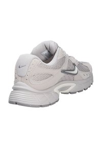 Zapatilla deportiva gris claro con paneles de malla, cuello acolchado, suela amortiguada y un pequeño logo gris oscuro en el lateral y el talón.