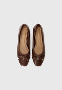 Ballerines en cuir marron avec un bout rond, ornées d'un petit nœud et de accents dorés à l'avant. Texture lisse, design décontracté.