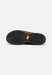 Čierna podrážka obuvi s textúrovaným gumovým vzorom, s logom Vibram, zvýraznená červeným akcentom okolo okraja.