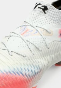 White soccer cleat with a textured upper, gradient red to blue design, and gray laces. Features a ribbed heel and logo on the tongue.
