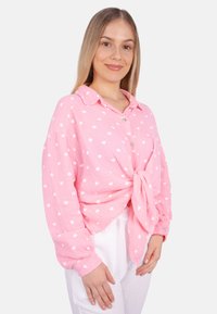 Rosa Hemd mit weißem Herzmuster, an der Taille geknotet, mit Kragen und langen Ärmeln mit Knopfakzenten.