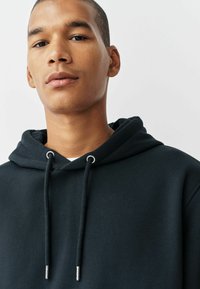 Schwarzer Hoodie mit verstellbaren Kordeln, ausgestattet mit silbernem Zubehör und einem glatten, strukturierten Stoff. Einfaches Design mit klassischer Passform.