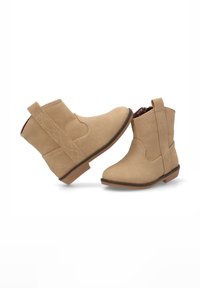 Botas de tobillo de ante color beige con un tacón corto y plano, costuras decorativas y paneles laterales elásticos para un fácil uso. Suela de goma marrón.