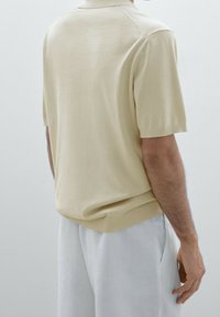 Beige polo shirt met korte mouwen, gemaakt van lichtgewicht stof, met een geribbelde zoom en een gladde textuur, gedragen met lichtgekleurde broeken.