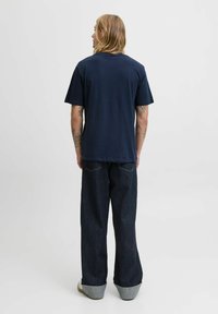 Marineblå bomulds-t-shirt med korte ærmer, afslappet pasform og ensartet design; båret med mørke denimjeans med opsmøg.