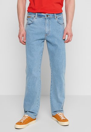 Jeans in denim azzurro chiaro con taglio dritto, cinque tasche e chiusura a bottone. Indossati con sneakers arancioni, dotate di lacci bianchi.