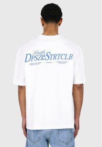 White t-shirt featuring a large blue graphic text on the back, with rounded neckline and short sleeves, paired with blue jeans.