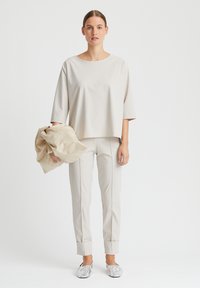 Hellbeige Oberteil mit weiten Ärmel, kombiniert mit passenden maßgeschneiderten Hosen. Das Outfit umfasst silberne Slipper und einen strukturierten beigen Schal.