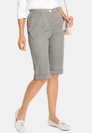 Pantaloni bermuda in lino grigio con chiusura a bottoni e cintura elastica. Comprendono risvolti e tasche laterali. Abbinati a mocassini bianchi.