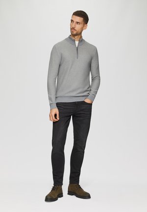 Šedý svetr s čtvrtovým zipem a texturou, kombinovaný s černými slim-fit džíny a hnědými šněrovacími botami na jednoduchém pozadí.