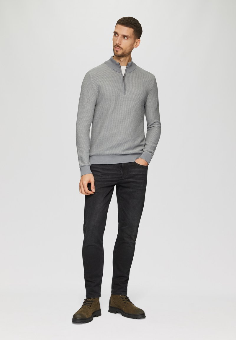 Grijze quarter-zip trui met een gestructureerd patroon, gecombineerd met zwarte slim-fit jeans en bruine veterschoenen op een effen achtergrond.