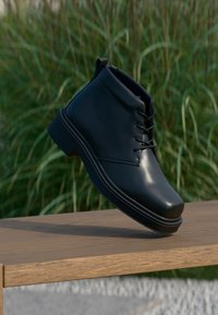 Black leather ankle boots with a smooth finish, round toe, lace-up design, and a sturdy flat sole, displayed on a wooden surface.