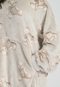 Prenda de forro polar color crema con un patrón de ositos de peluche y pequeños corazones. El material parece suave y texturizado. Detalle de puño visible.