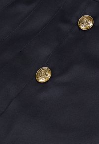 Navy-Blau Stoffnahaufnahme mit zwei goldenen Knöpfen im Totenkopfdesign und filigranen Details, glatte Textur und genähte Nähte.