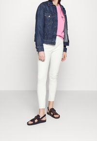 Denim jacket, pink sweatshirt, white skinny jeans, and dark brown sandals with a strap and fringe detail. Casual outfit with complementary colors.