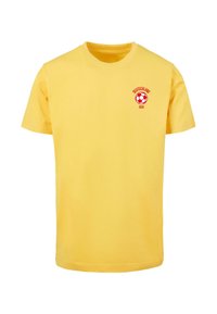 Žluté bavlněné tričko s červenou grafikou obsahující fotbal, nápis "DEUTSCHLAND" a "2024" vytištěný na levé části hrudi. Standardní střih.