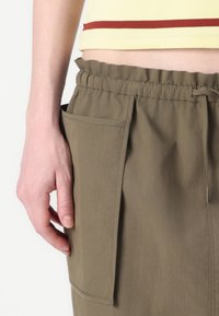 Olivengrønne bukser med elastisk talje, med en sidelomme. Stof virker let med en glat tekstur og et enkelt design.