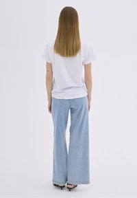 Valkoinen puuvillainen t-paita lyhyillä hihoilla yhdistettynä vaaleansinihin leveälahkeisiin farkkuihin. Farkuissa on repsottava helma ja hieno haalistuminen.