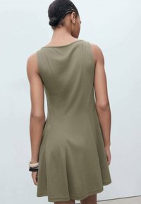 Rochie verde măslinie, cu fustă evazată, confecționată dintr-un material neted, cu un design fără mâneci și decolteu rotund, evidențiind detalii cusute pe spate.