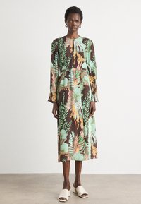 Abito lungo a maniche, floreale con uno sfondo marrone, decorato con motivi botanici verdi e arancioni, tessuto testurizzato, lunghezza sopra la caviglia, vestibilità comoda.