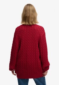 Pull rouge en tricot avec motifs torsadés texturés, coupe oversize, manches longues et ourlet en côte. Vue de dos.