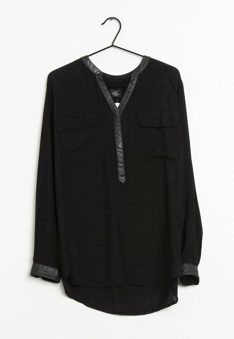 Blouse noire à manches longues avec bordure en cuir synthétique sur le col, la patte de boutonnage et les poignets, avec deux poches poitrine, suspendue sur un cintre noir.