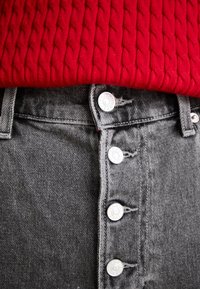 Jeans de mezclilla gris de cintura alta con cinco botones, que cuentan con herrajes plateados. La cintura se combina con un suéter de punto texturizado rojo.