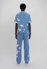 Μπλε σετ που περιλαμβάνει μπλούζα με λευκά αστέρια και λευκές λεπτομέρειες, καθώς και παντελόνια σε χαλαρή εφαρμογή με αστέρια στα πόδια. Μαλακή υφή, casual σχέδιο.