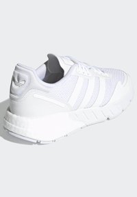 Biele atletické topánky vyrobené z sieťoviny a syntetických materiálov. Majú tri biele pruhy, textúrovaný zvršok a podrážku s tlmením.