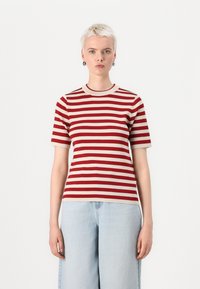 Camicia a maniche corte a righe rosse e beige con scollatura rotonda, realizzata in tessuto a costine, caratterizzata da una forma aderente. Abbinata a jeans azzurri chiari.