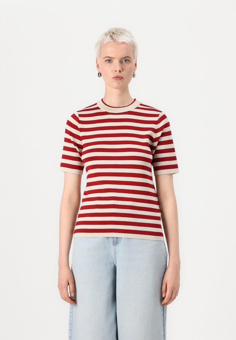 Camicia a maniche corte a righe rosse e beige con scollatura rotonda, realizzata in tessuto a costine, caratterizzata da una forma aderente. Abbinata a jeans azzurri chiari.