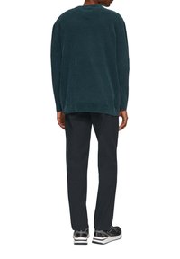 Donkerblauwe geribbelde trui met een ronde hals, gedragen over zwarte broek en zwarte sneakers met witte accenten. Casual en ontspannen pasvorm.
