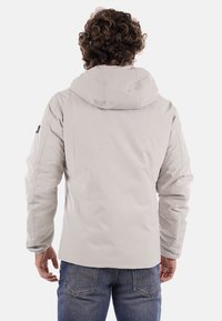 Chaqueta gris claro con capucha, textura suave y mangas largas; presenta un logo en la manga izquierda y un corte casual.